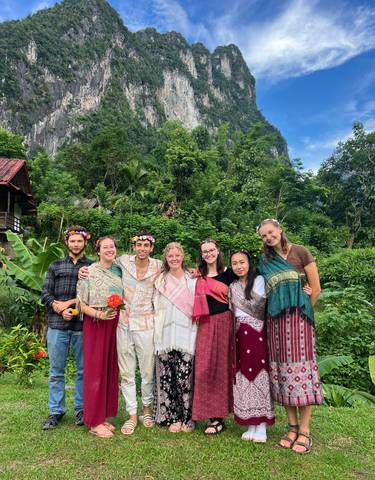 Group of people dressed in traditional attire posing with a lush green mountain background.