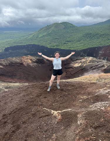 Person standing on the edge of a volcanic crater, arms outstretched.