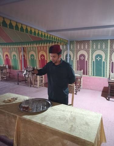 A man in traditional attire pouring tea at a colorful restaurant.