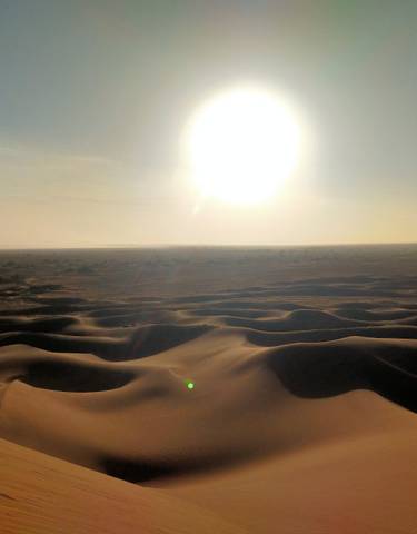 Desert landscape with sun setting over the dunes.