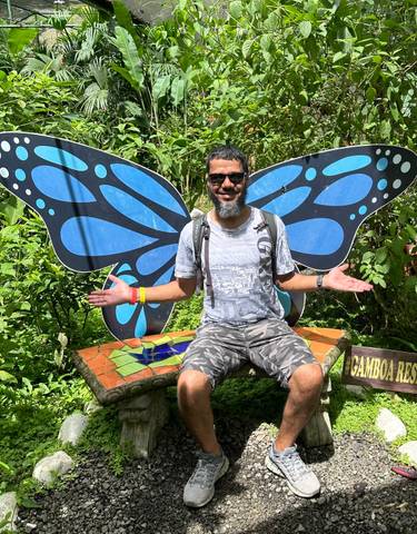 Man seated in front of decorative butterfly wings in a garden.