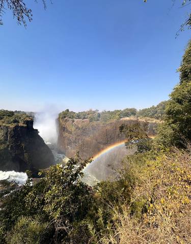 A scenic view of a waterfall with a rainbow over cliffs.