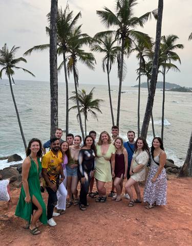 Group of people posing in front of palm trees with the ocean in the background.