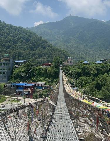 Suspension bridge with flags and buildings in the background in Nepal.