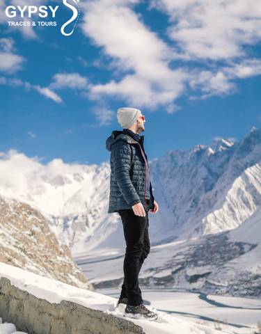 Person in winter clothing looking at snow-capped mountains.