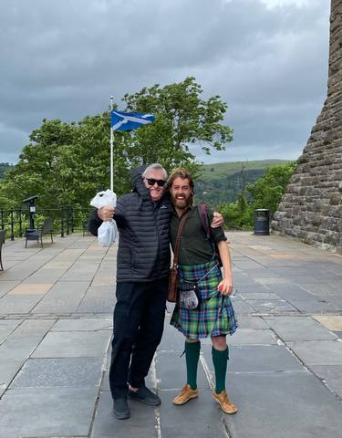 Two men happily posing outdoors with scenic greenery.