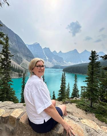 Woman posing with a scenic view of a lake and mountains.