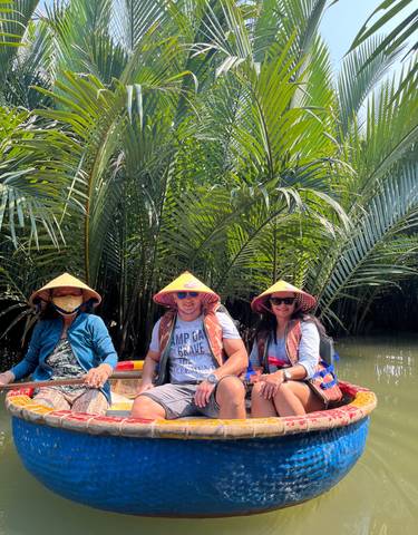 Group of people wearing conical hats posing in a boat with lush greenery.