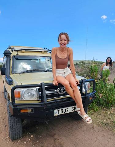 Person sitting on the hood of a safari vehicle with sparse vegetation around.