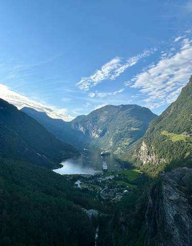 A panoramic view of a fjord with boats and steep mountains.