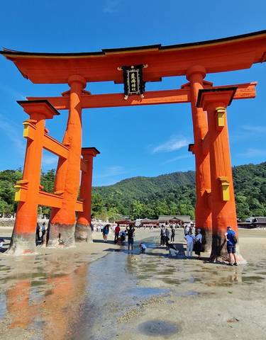 Large red torii gate in water with people nearby.