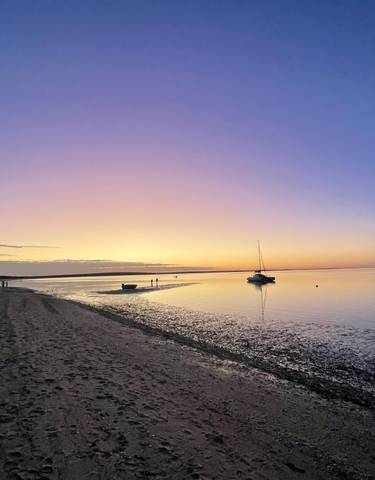 Sunset over a calm sea with boats and people silhouetted.