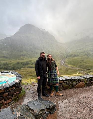 Two people posing with a scenic mountain view on a cloudy day.