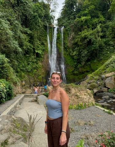 Woman posing near a waterfall with lush greenery.