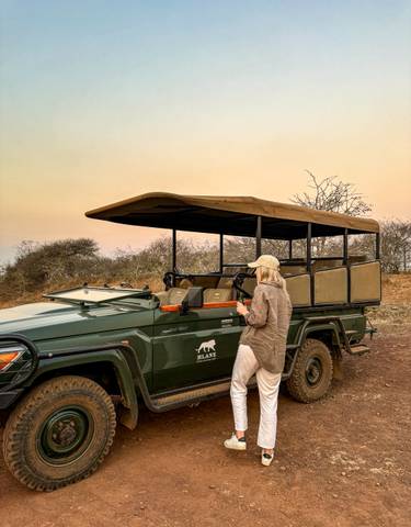 Person standing next to a safari vehicle at sunset.