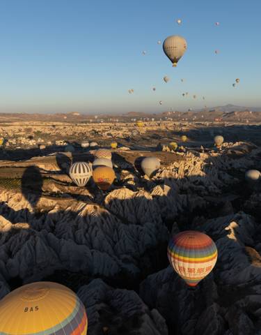 Numerous hot air balloons over a rugged terrain at dawn.