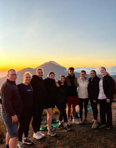 Group of people posing during sunrise with mountains in the background.
