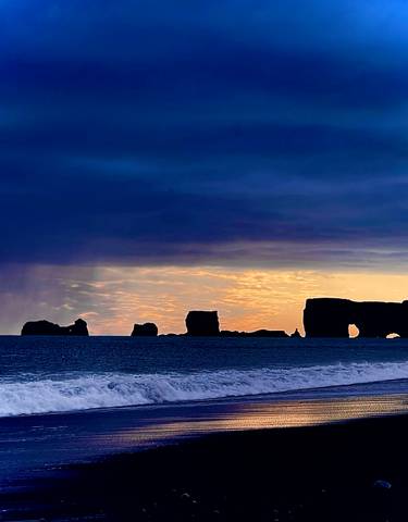 Silhouette of sea stacks at dusk against a colorful sky.