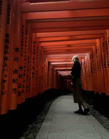 Person walking through a path lined with red torii gates with inscriptions