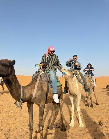 Group of people riding camels in a desert landscape.