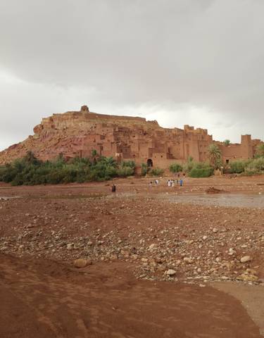 Ancient kasbah with people in the foreground on a rocky terrain.