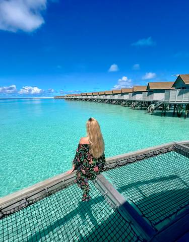 A woman sitting by overwater bungalows in clear turquoise water.
