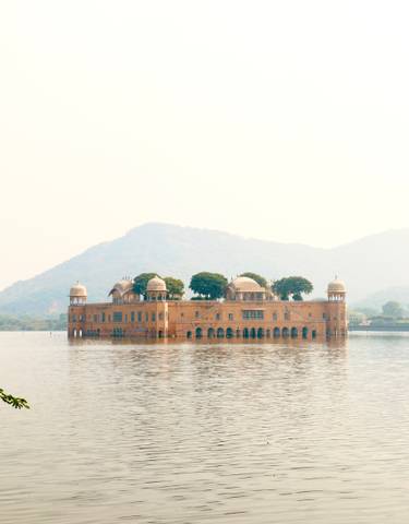 Jal Mahal palace located in the middle of a lake with mountains in the background.