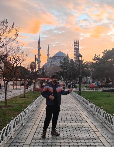 A man posing in front of a mosque during sunset.