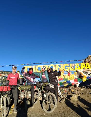 Cyclists posing at the summit of a mountain pass with flags and sign.