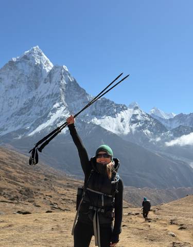 Woman celebrating with trekking poles in front of snowy mountains.