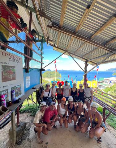 Group of people with harnesses at zipline station overlooking the sea.