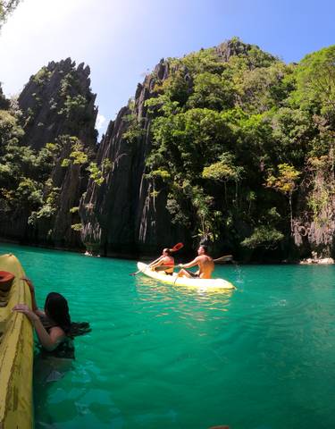 Two people kayaking on turquoise water surrounded by steep cliffs.