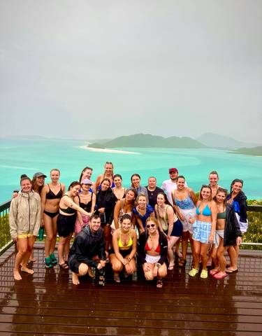 A large group posing with a view of turquoise waters, likely on an island.