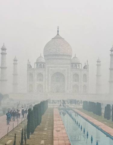 View of the Taj Mahal shrouded in mist with people in the foreground.