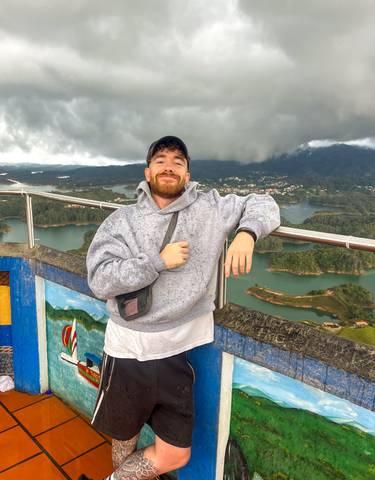 A man posing with a scenic view of Guatape behind.