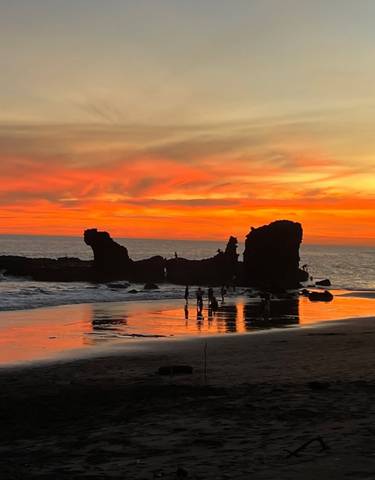 A beach during sunset with silhouettes of people and rocks.