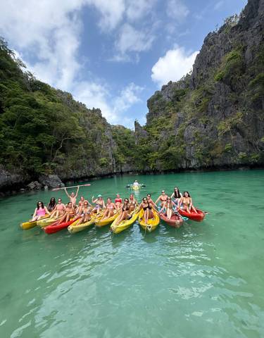 Large group of people on kayaks in clear turquoise water with limestone cliffs.