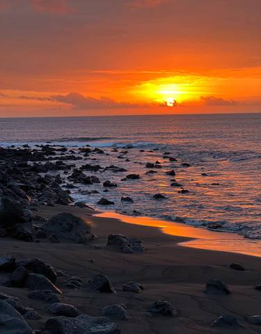 Rocky shoreline with waves and a sunset over the ocean.