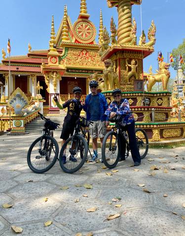 Three people with bicycles posing in front of an ornate temple.