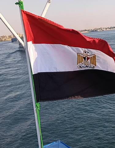 Egyptian flag waving on a ship with a river scene.