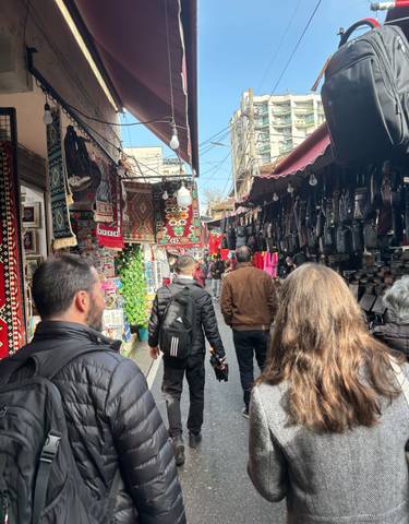 Market alley with people and colorful textiles hanging.