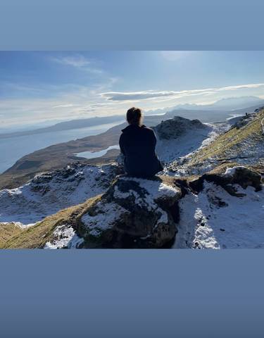 Person sitting on a snowy mountain overlooking a loch.