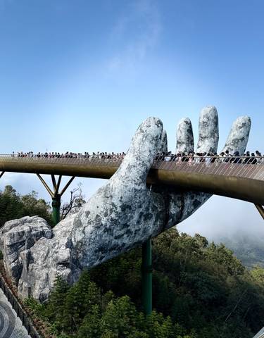 Golden Bridge with a giant stone hand sculpture and tourists walking across.