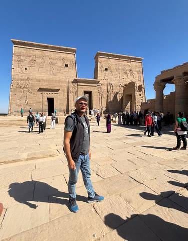 Person standing in front of ancient temple ruins with people around.