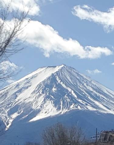 Snow-capped Mount Fuji under a blue sky with clouds.