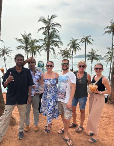 Group of six people standing in front of a beach with palm trees.
