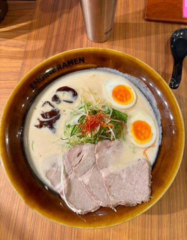 Bowl of ramen with sliced meat, eggs, and vegetables.