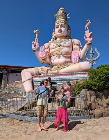 Two people posing in front of a large pink Hindu deity statue.