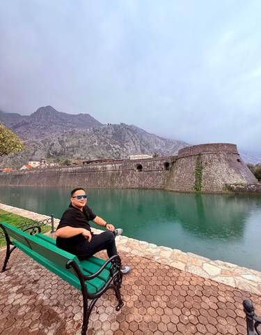 Tourist sitting by a scenic water body with fortifications.