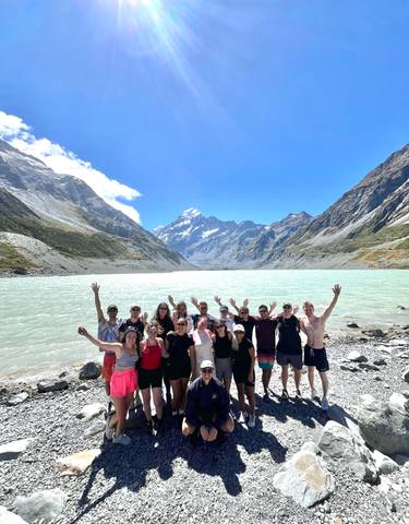 Group of people posing with arms raised before a stunning mountainous landscape.
